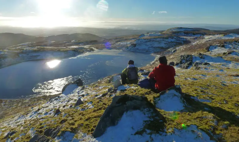 Two people sitting on a hill in the snow.